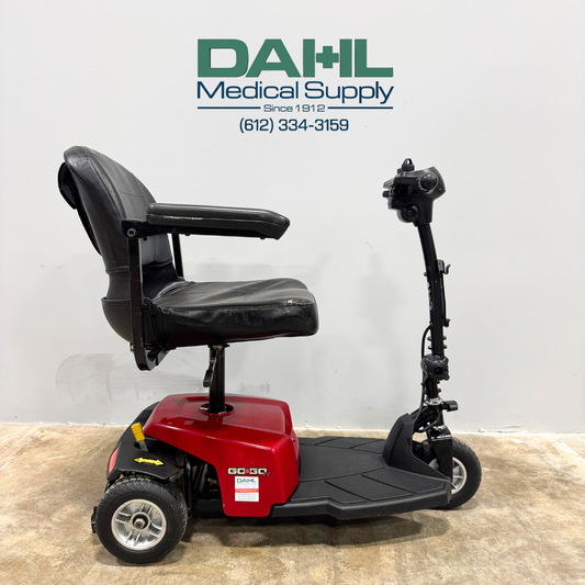 Side view of a used Pride Go-Go ES 3-wheel mobility scooter featuring a compact red base, black swivel seat with armrests, and adjustable tiller, photographed inside Dahl Medical Supply.