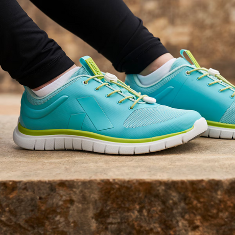 Woman wearing teal and lime green diabetic athletic shoes with cushioned white soles and breathable mesh design for comfort and support – available at Dahl Medical Supply.