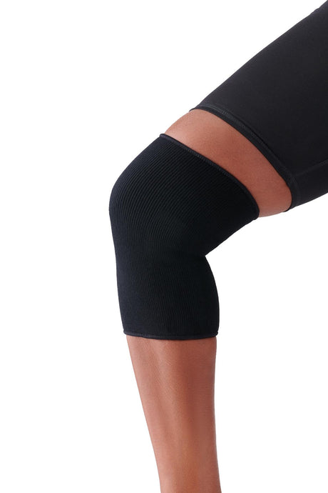 Person wearing a black knee support sleeve for joint stability and compression—extremity support product available at Dahl Medical Supply.