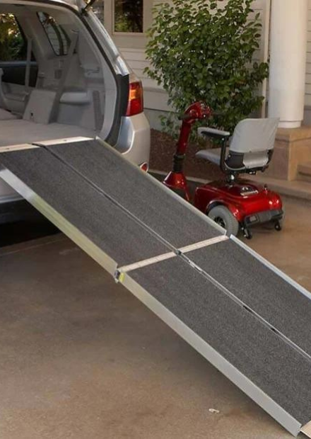 Aluminum folding ramp leading into a vehicle with a red mobility scooter nearby, illustrating a portable ramp rental available from Dahl Medical Supply.