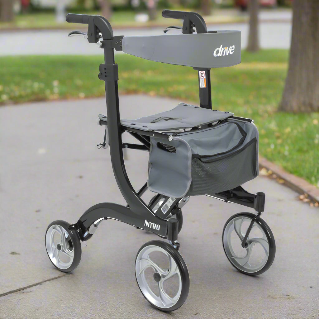 Drive Medical Nitro Aluminum Tall Rollator (RTL10266BK-T) shown outdoors on a paved sidewalk, featuring black lightweight frame, 10-inch wheels, padded seat, and storage bag.