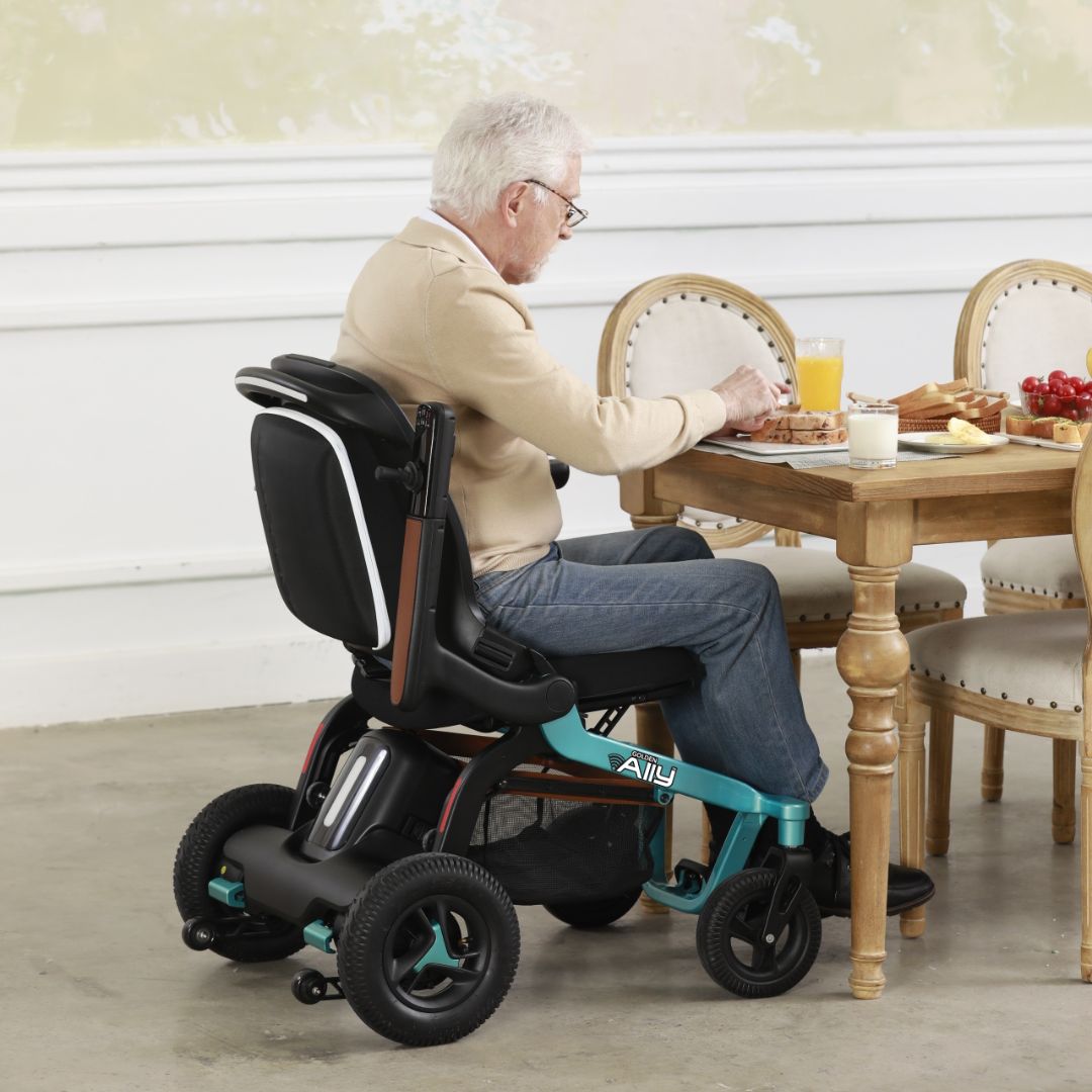 Adult seated in a Golden Ally GP303 portable power wheelchair while dining at a table indoors, showing the compact frame, comfortable seating, and easy maneuverability.
