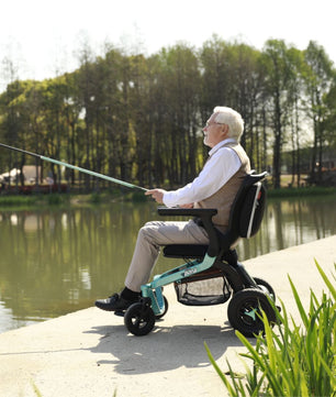 Adult using a Golden Ally GP303 portable power wheelchair while fishing beside a calm lake, with trees and nature in the background.