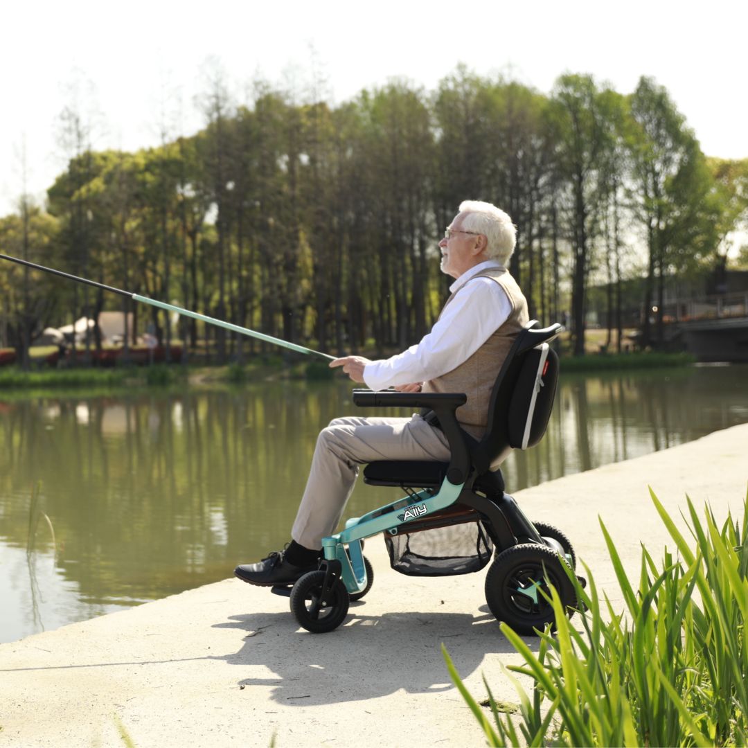 Adult using a Golden Ally GP303 portable power wheelchair while fishing beside a calm lake, with trees and nature in the background.