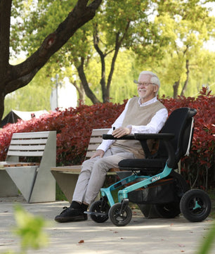 Adult seated comfortably in a Golden Ally GP303 portable power wheelchair outdoors, enjoying a park setting with trees, benches, and bright foliage in the background.