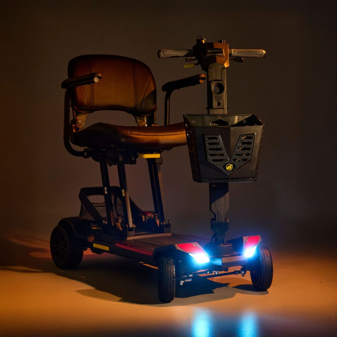 Golden Buzzaround CarryOn GB120 travel scooter with LED headlights turned on.
