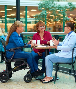 Woman using the Golden Cricket Powerchair getting coffee with friends, showcasing how compact it is.