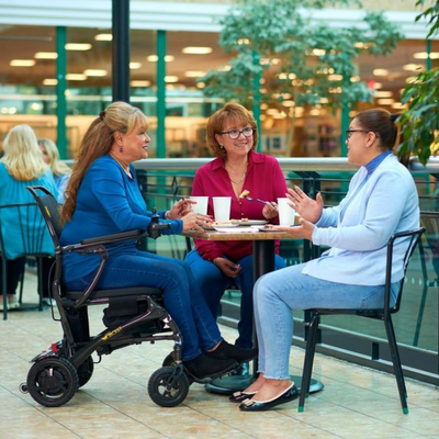 Woman using the Golden Cricket Powerchair getting coffee with friends, showcasing how compact it is.