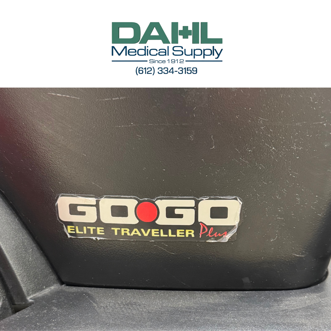 Close-up view of the battery compartment on a used Pride Go Go Elite Traveller Plus 3-wheel mobility scooter, showing the Go Go Elite Traveller Plus branding.