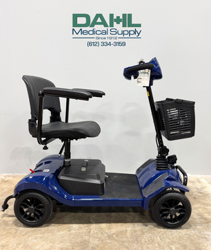 Blue used 4-wheel mobility scooter shown from the side, featuring a padded seat, armrests, front basket, and compact design, photographed inside Dahl Medical Supply.