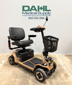 Angled view of a used Baja Bandit 4-wheel mobility scooter featuring a padded swivel seat, front basket, rugged tires, and tan-and-black frame, photographed in the Dahl Medical Supply showroom.
