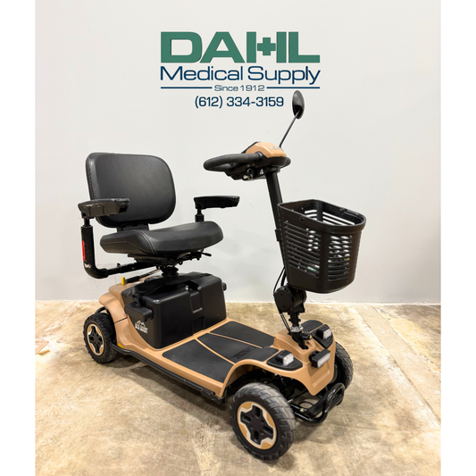 Angled view of a used Baja Bandit 4-wheel mobility scooter featuring a padded swivel seat, front basket, rugged tires, and tan-and-black frame, photographed in the Dahl Medical Supply showroom.