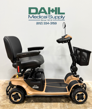 Side profile of a used Baja Bandit 4-wheel mobility scooter showing wide foot platform, adjustable seat with armrests, heavy-duty wheels, and stable outdoor-ready design from Dahl Medical Supply.