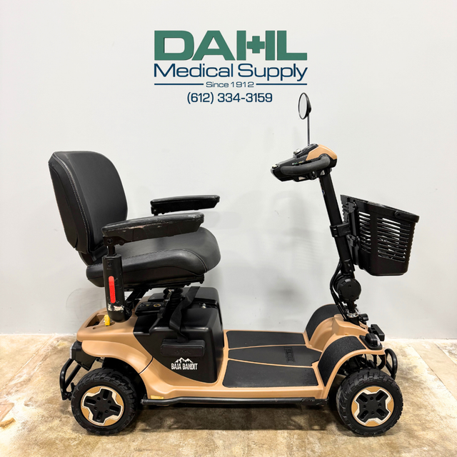Side profile of a used Baja Bandit 4-wheel mobility scooter showing wide foot platform, adjustable seat with armrests, heavy-duty wheels, and stable outdoor-ready design from Dahl Medical Supply.