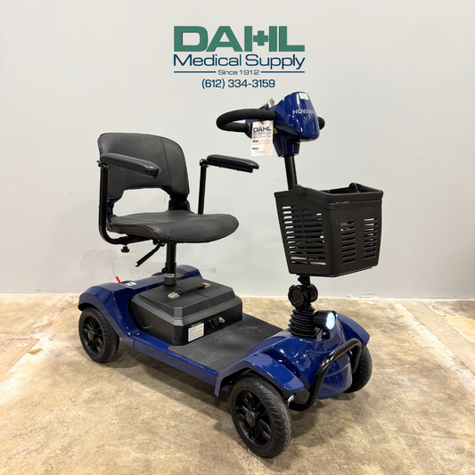 Angled front view of a blue used 4-wheel mobility scooter with front basket, padded seat, and black wheels, displayed indoors at Dahl Medical Supply.