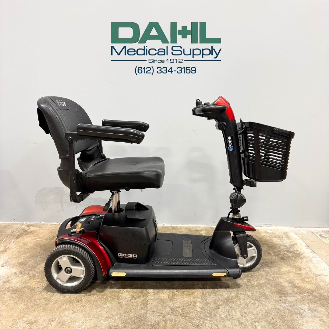 Side view of a used Pride Go Go Elite Traveller Plus 3-wheel mobility scooter with padded seat, armrests, front basket, and compact frame, photographed at Dahl Medical Supply.